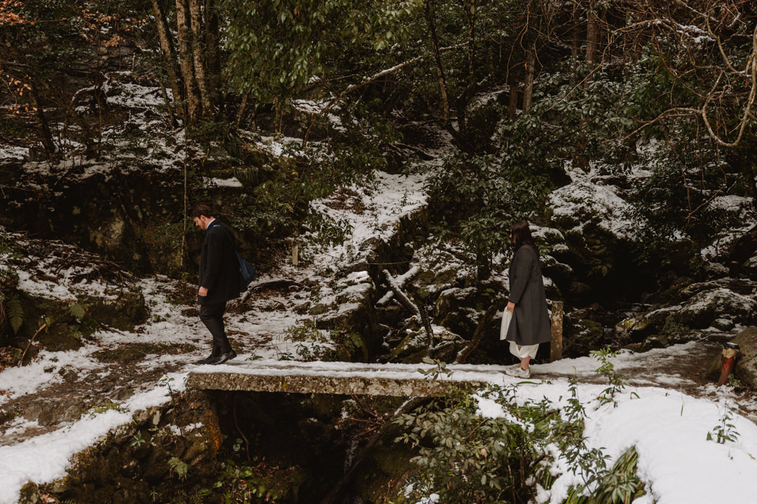 The couple hikes to get to the waterfall. Snow Shrine Elopement in Japan